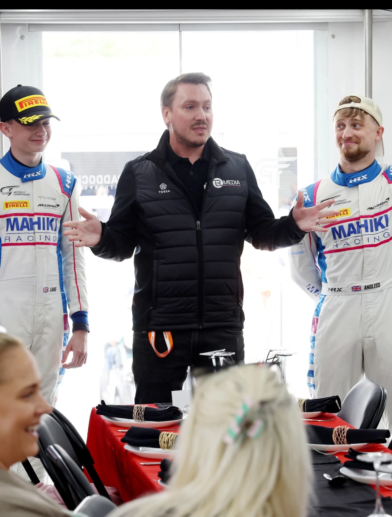 Two Mahiki Racing drivers in helmets and race suits waiting in the pit lane
