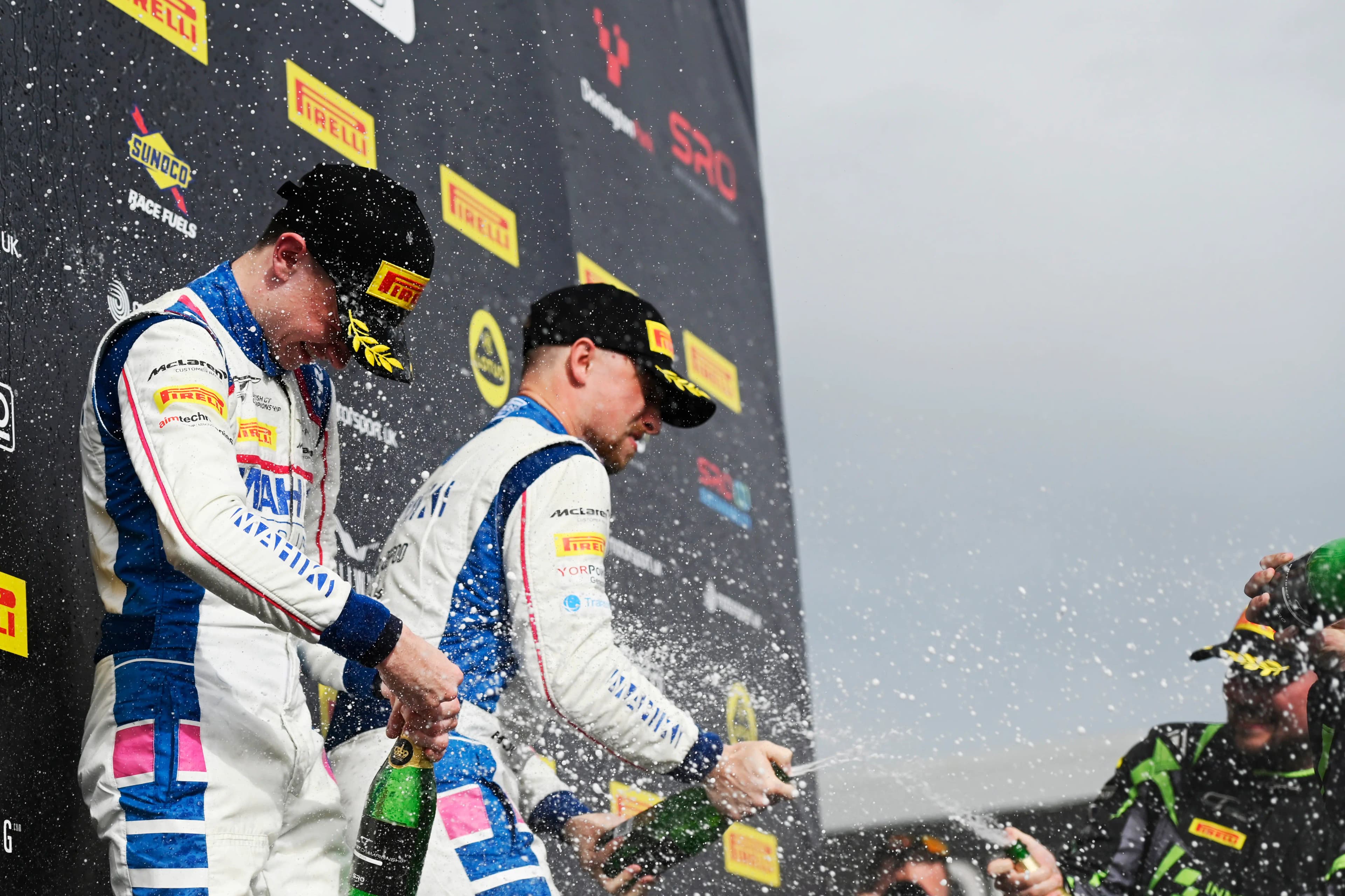 Revie Lake and Blake Angliss spraying champagne in their Mahiki Racing overalls on the Donington Park podium