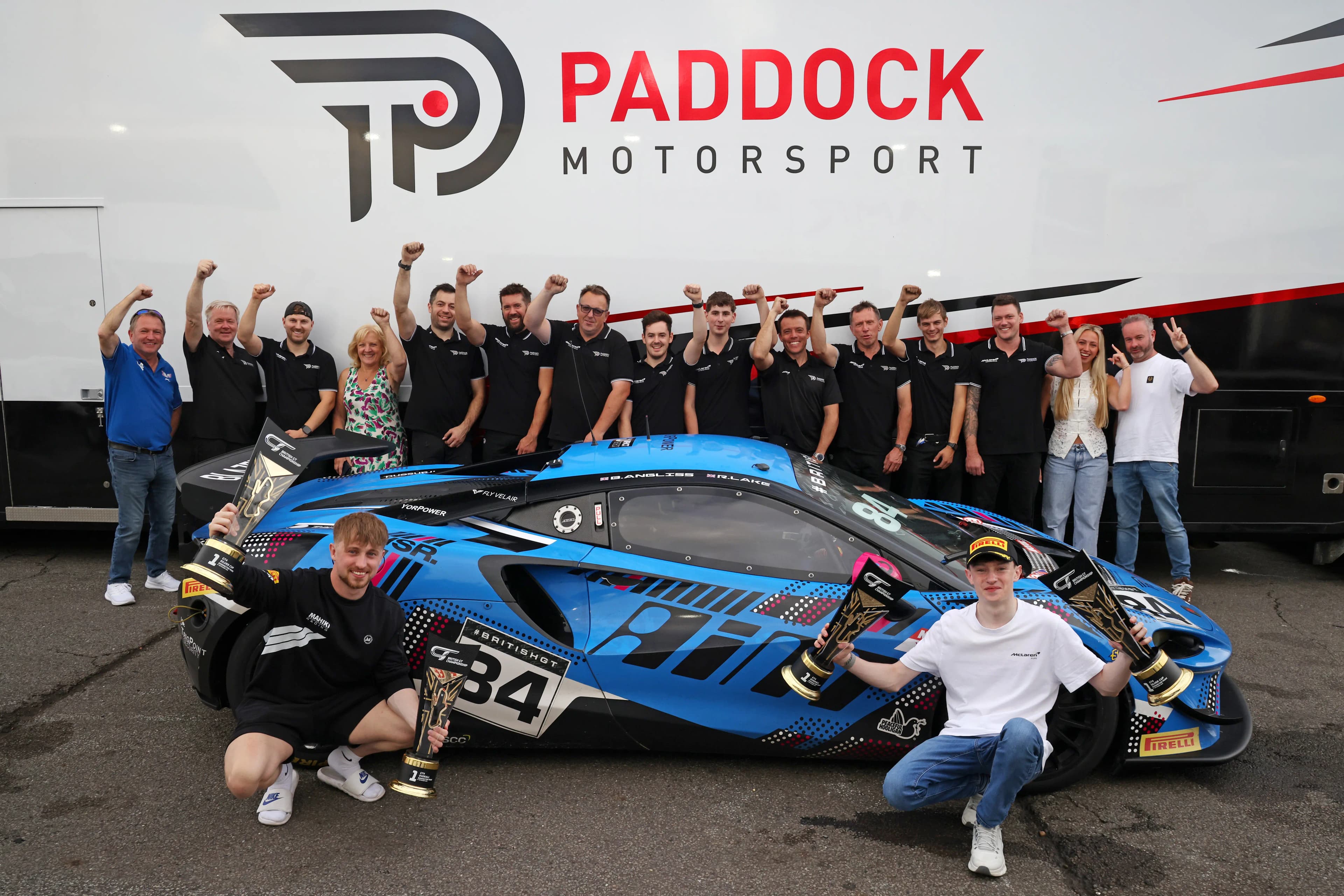Revie Lake, Blake Angliss and the Paddock Motorsport crew celebrating with their trophies in front of the number 84 McLaren Artura GT4 at Donington Park