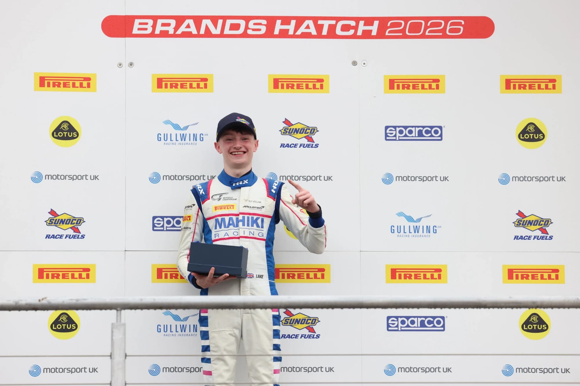 Revie Lake in Mahiki Racing overalls holding his trophy and raising one finger in front of the Brands Hatch 2026 backdrop