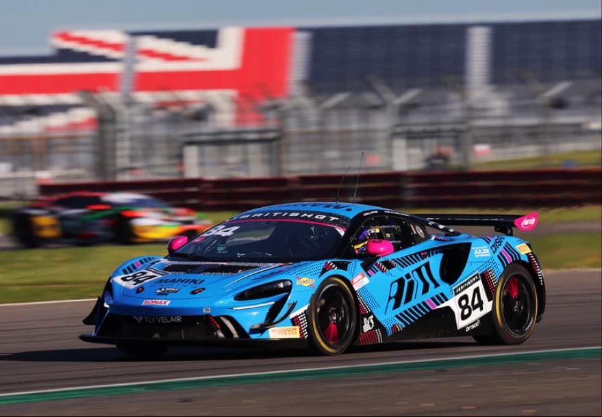 Revie Lake, helmeted and connected to the radio, leaning into the number 84 McLaren Artura GT4 in the garage