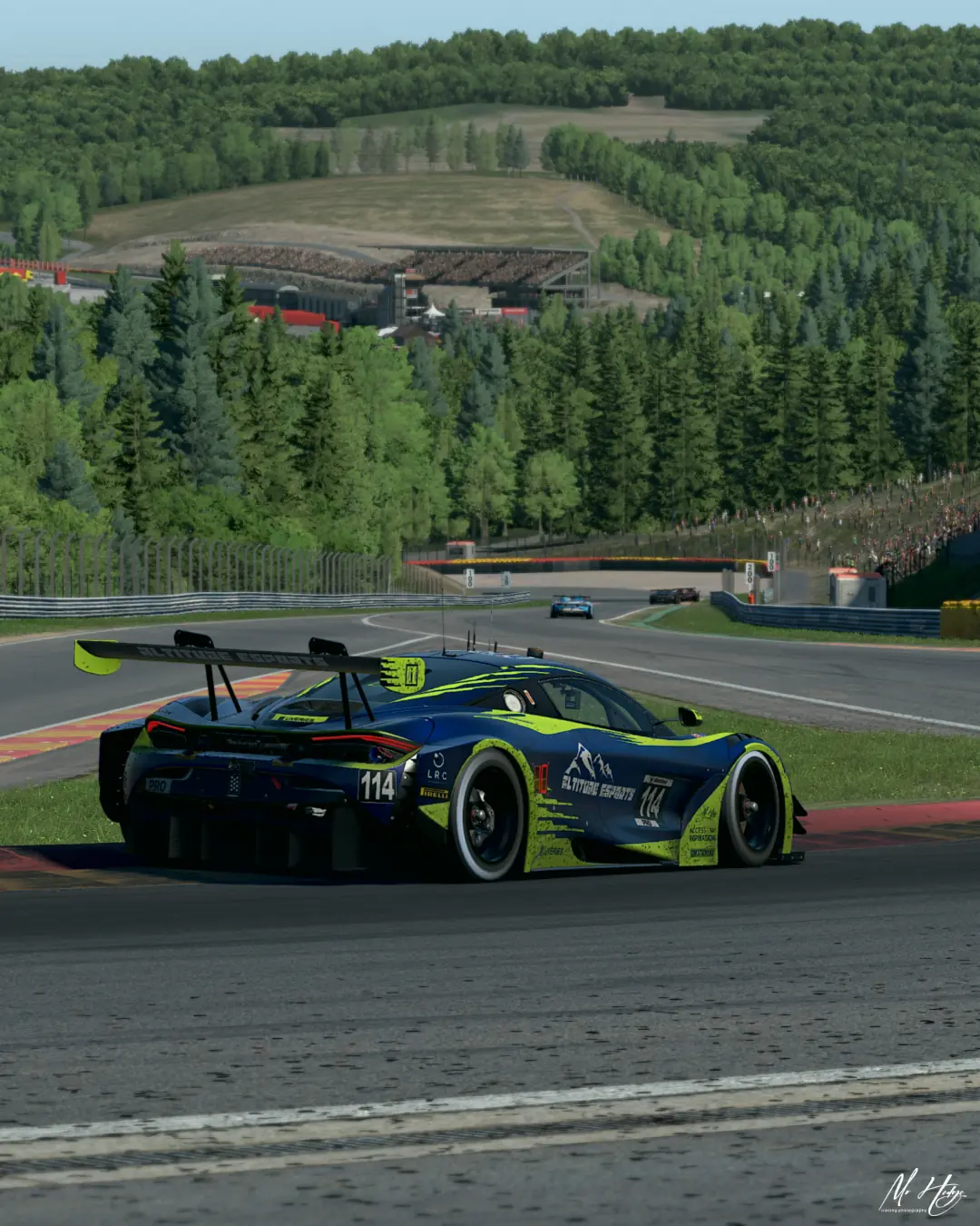The number 114 Altitude Esports McLaren 720S GT3 on the kerbs with the wooded Spa-Francorchamps hillside behind